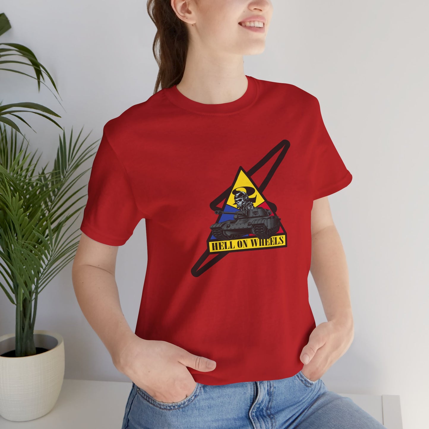 Person wearing a red t-shirt with a graphic design, sitting indoors next to a plant.