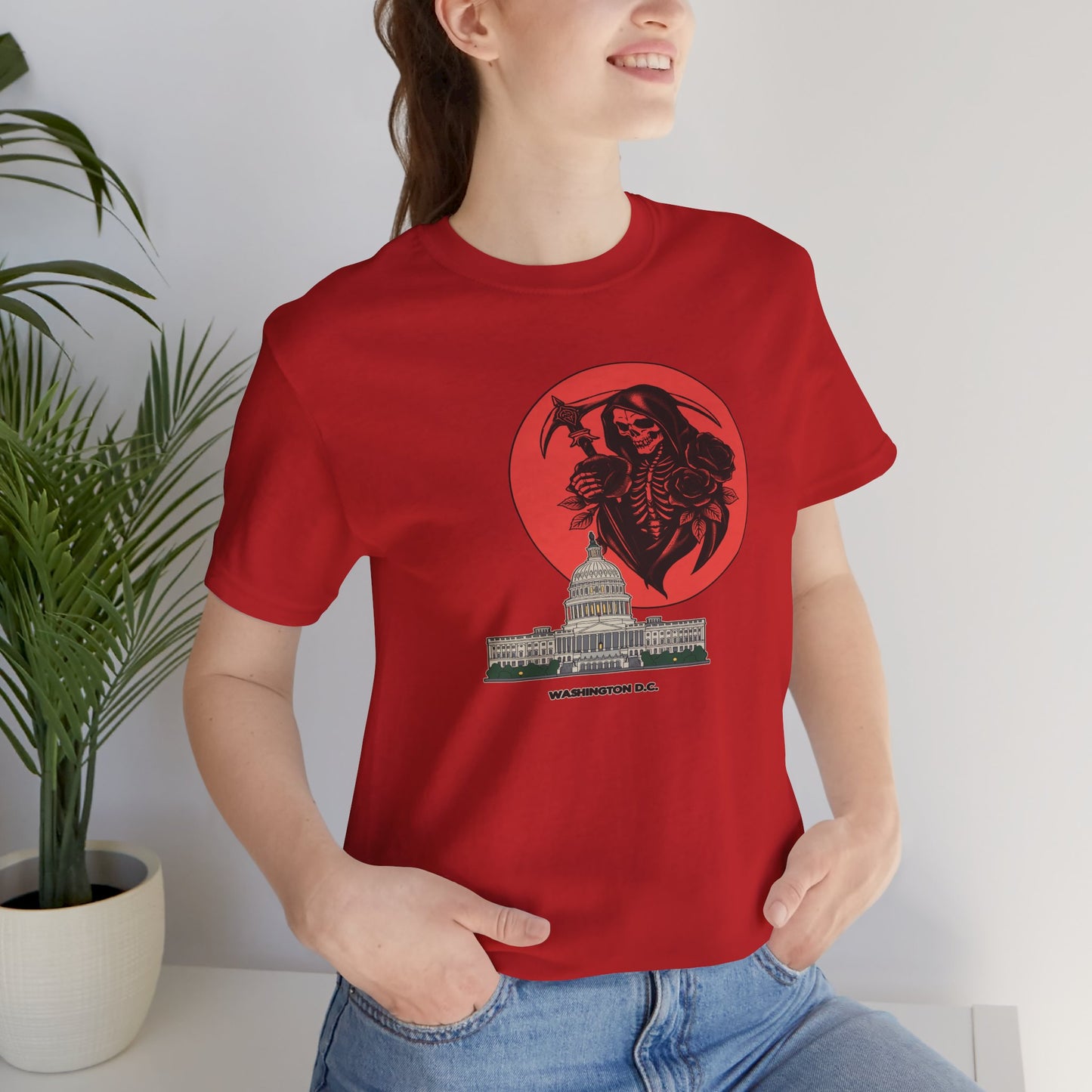 Person wearing a red t-shirt with a graphic design of a skeleton holding an axe over a building, standing indoors.