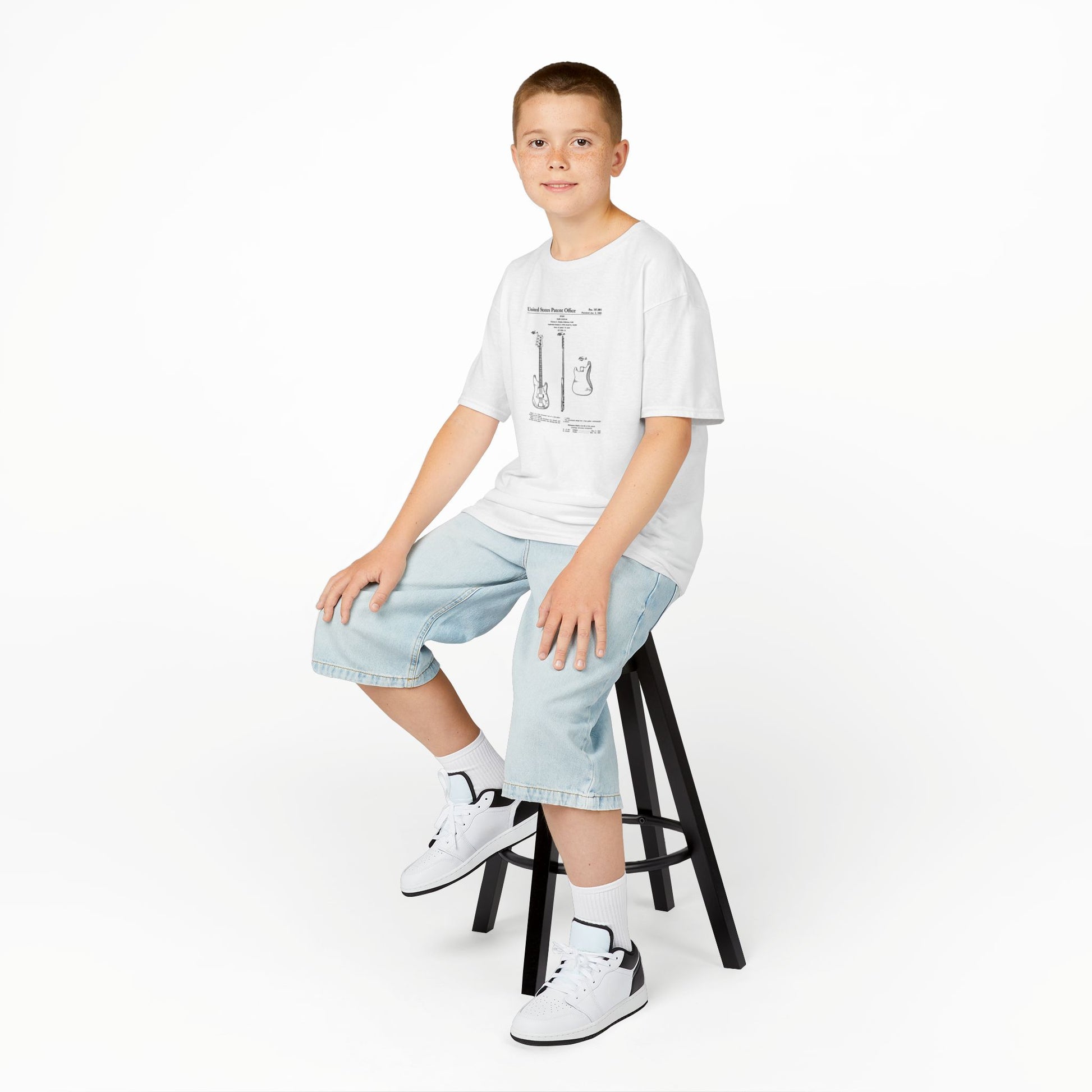 Young person sitting on a stool wearing a white t-shirt and light blue jeans against a white background