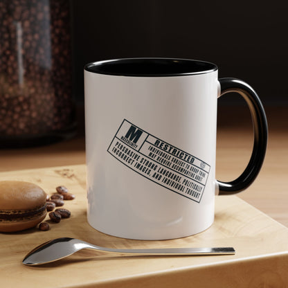White mug with black interior and handle, featuring a restricted label, on a wooden surface with coffee beans and a spoon.