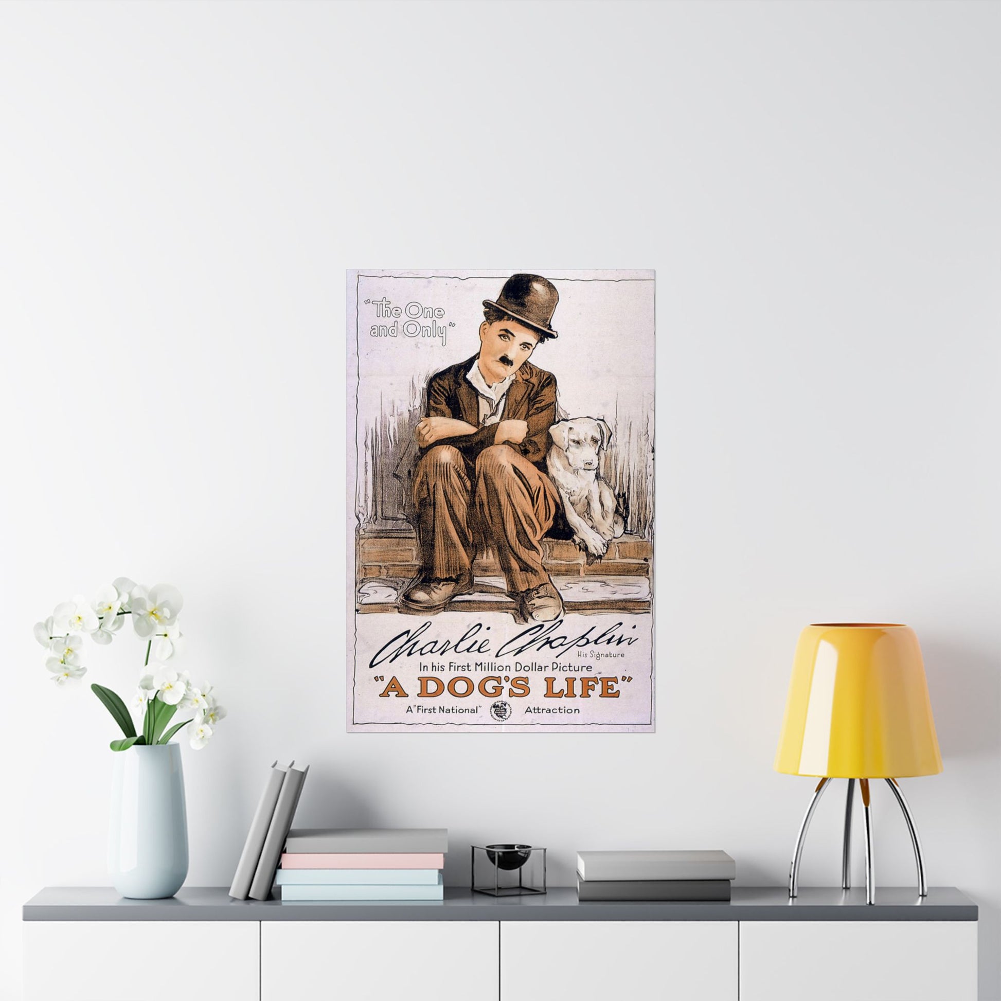 Poster of Charlie Chaplin and a dog on a wall above a shelf with books and a lamp.