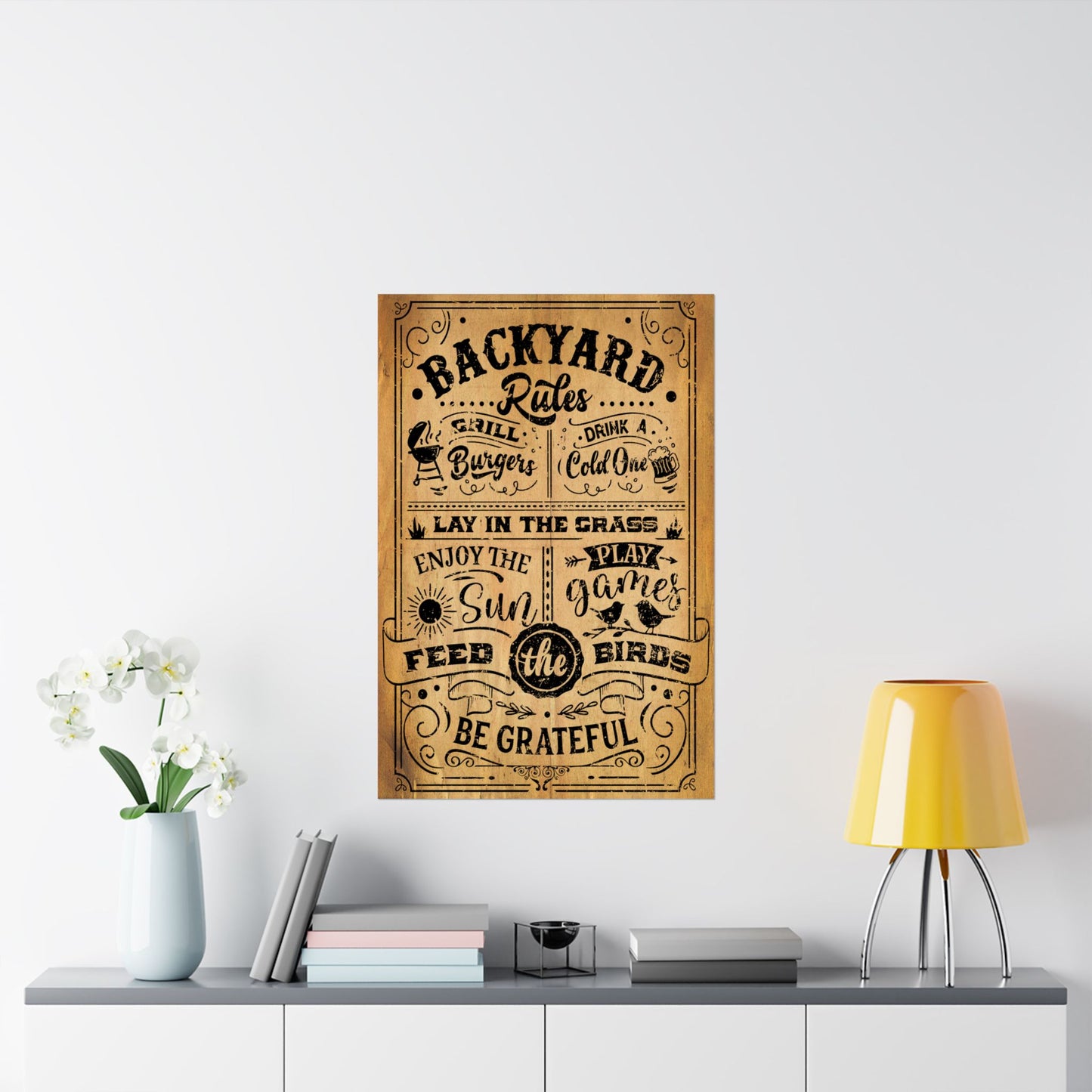 Decorative poster titled 'Backyard Rules' on a wall above a shelf with a lamp and books.