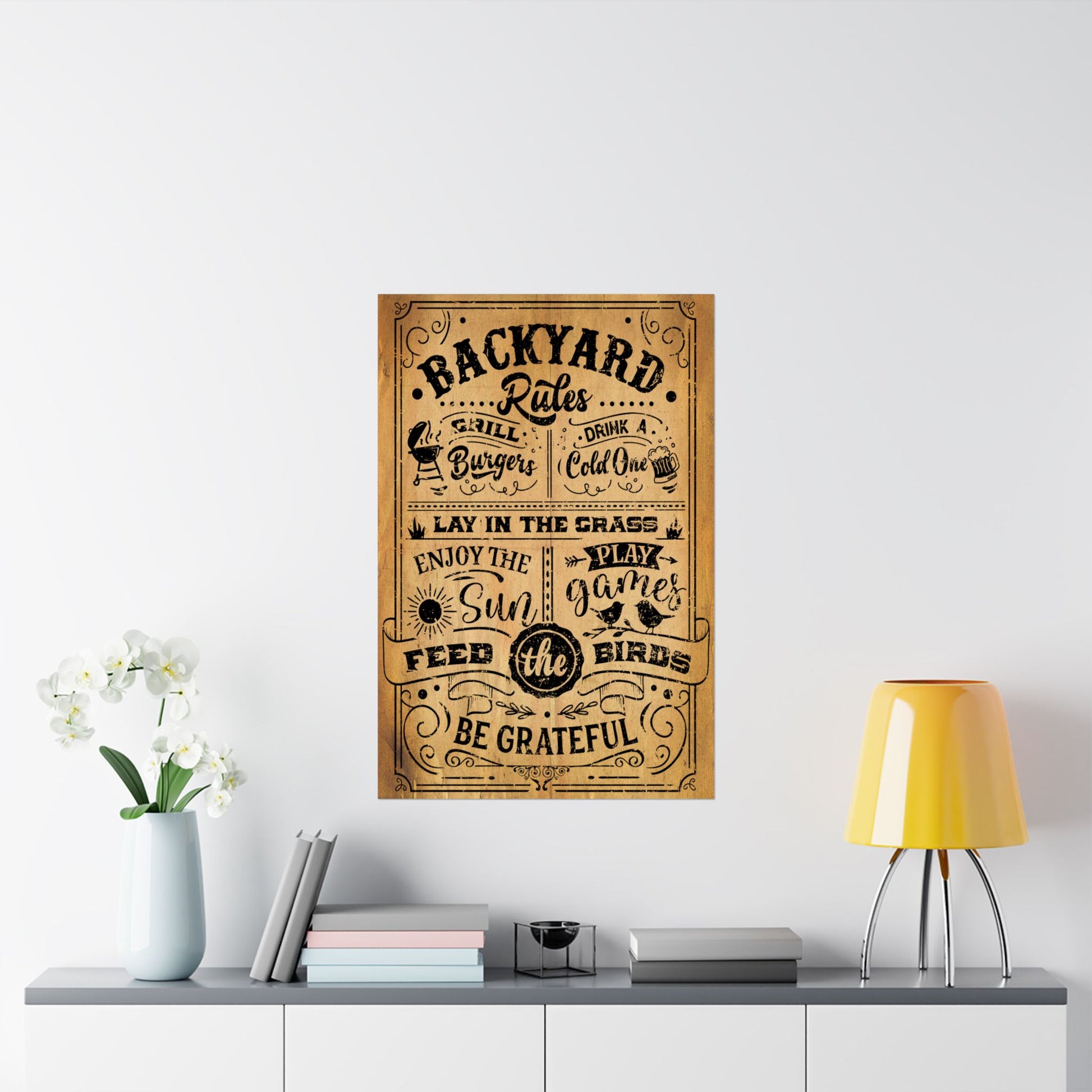 Decorative poster titled 'Backyard Rules' on a wall above a shelf with a lamp and books.