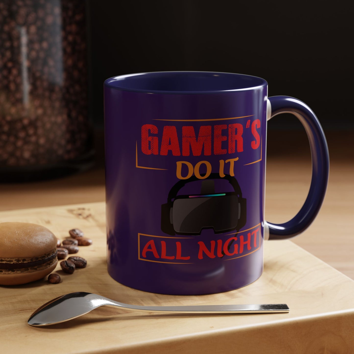 Blue mug with 'Gamer's do it all night' text on a wooden surface with coffee beans and a macaron.