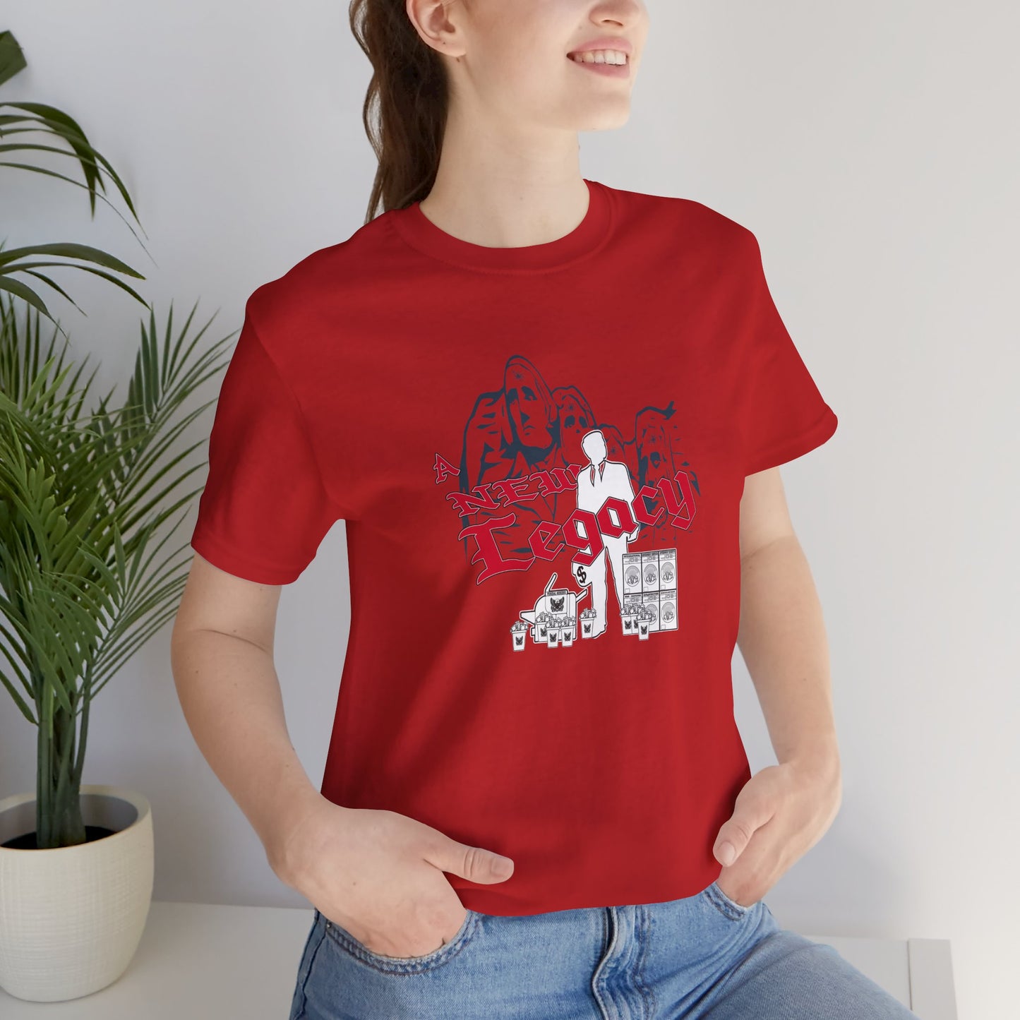 Person wearing a red t-shirt with graphic design, sitting indoors next to a plant.