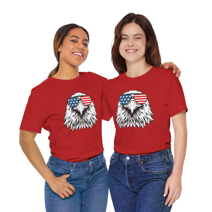 Two people wearing red t-shirts with an eagle graphic and American flag sunglasses on a white background.