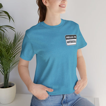 Person wearing a blue t-shirt with a patch that says 'Hello, I'm Antisocial' in a minimal indoor setting.