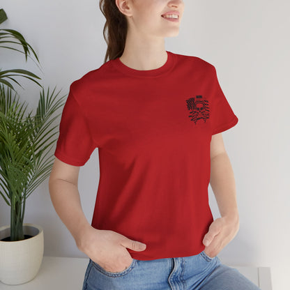 Person wearing a red t-shirt with a black design, standing indoors next to a plant.