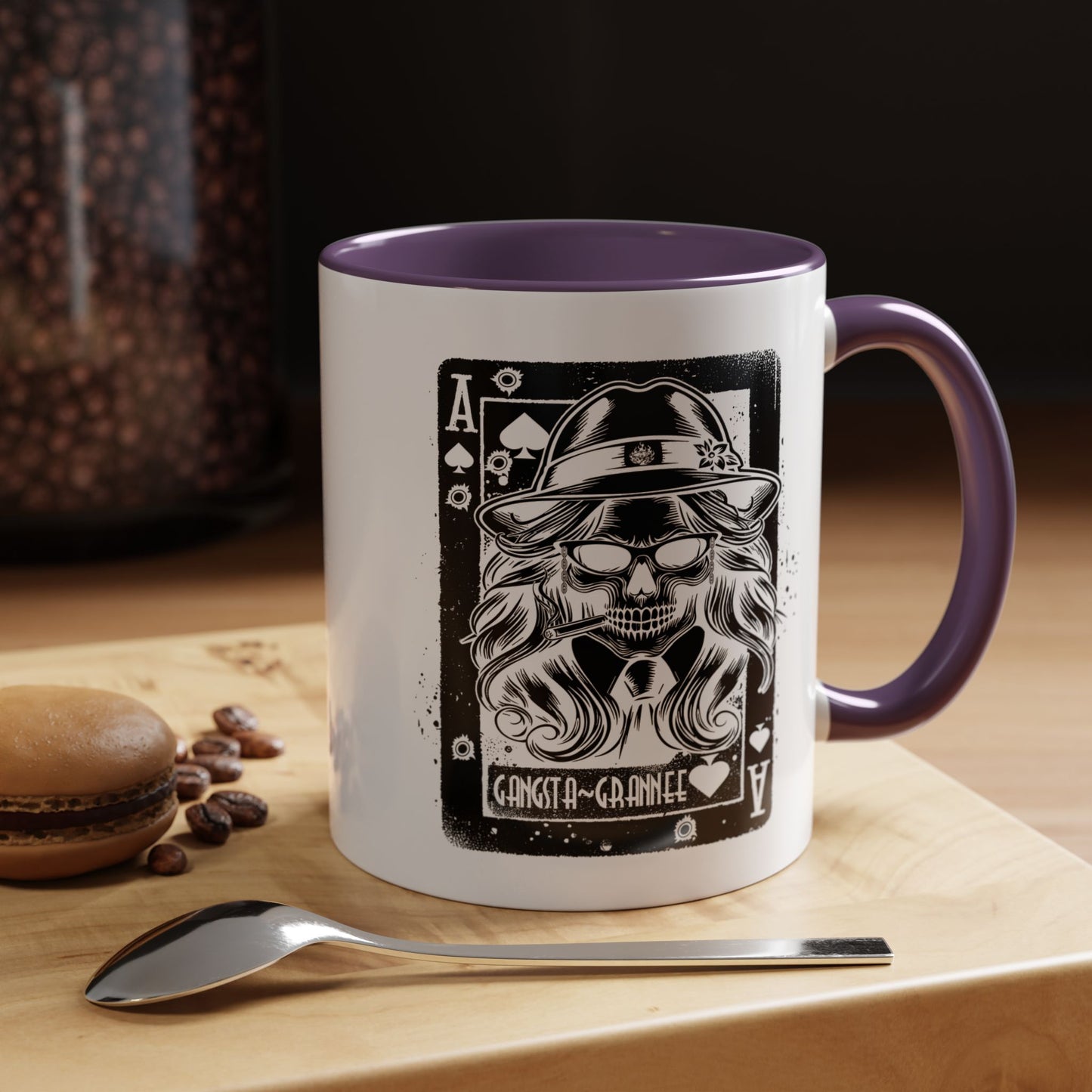 White mug with purple interior and handle featuring a skull design on a wooden surface with coffee beans and a spoon.