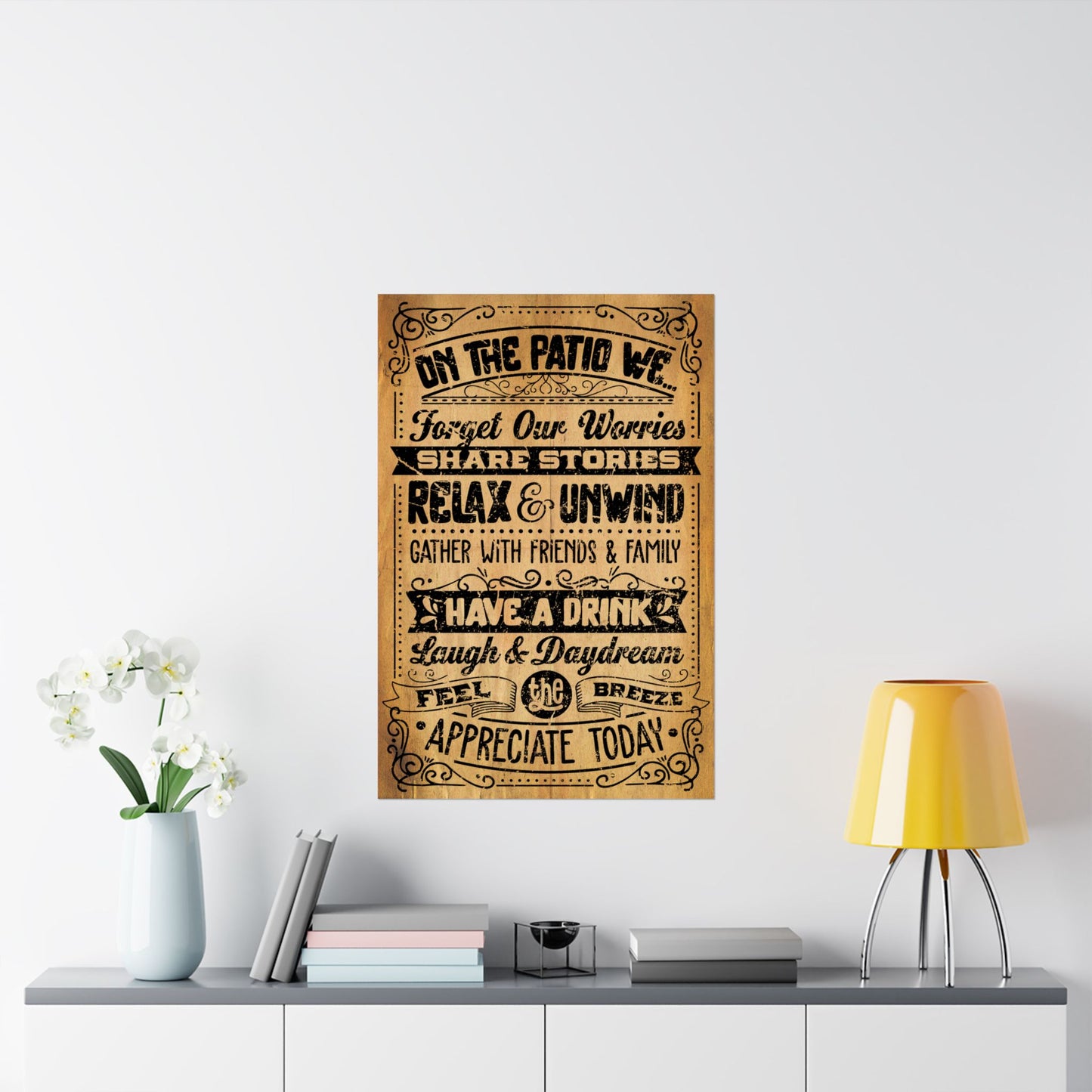 Decorative wall poster with text on a white wall above a shelf with books and a lamp.