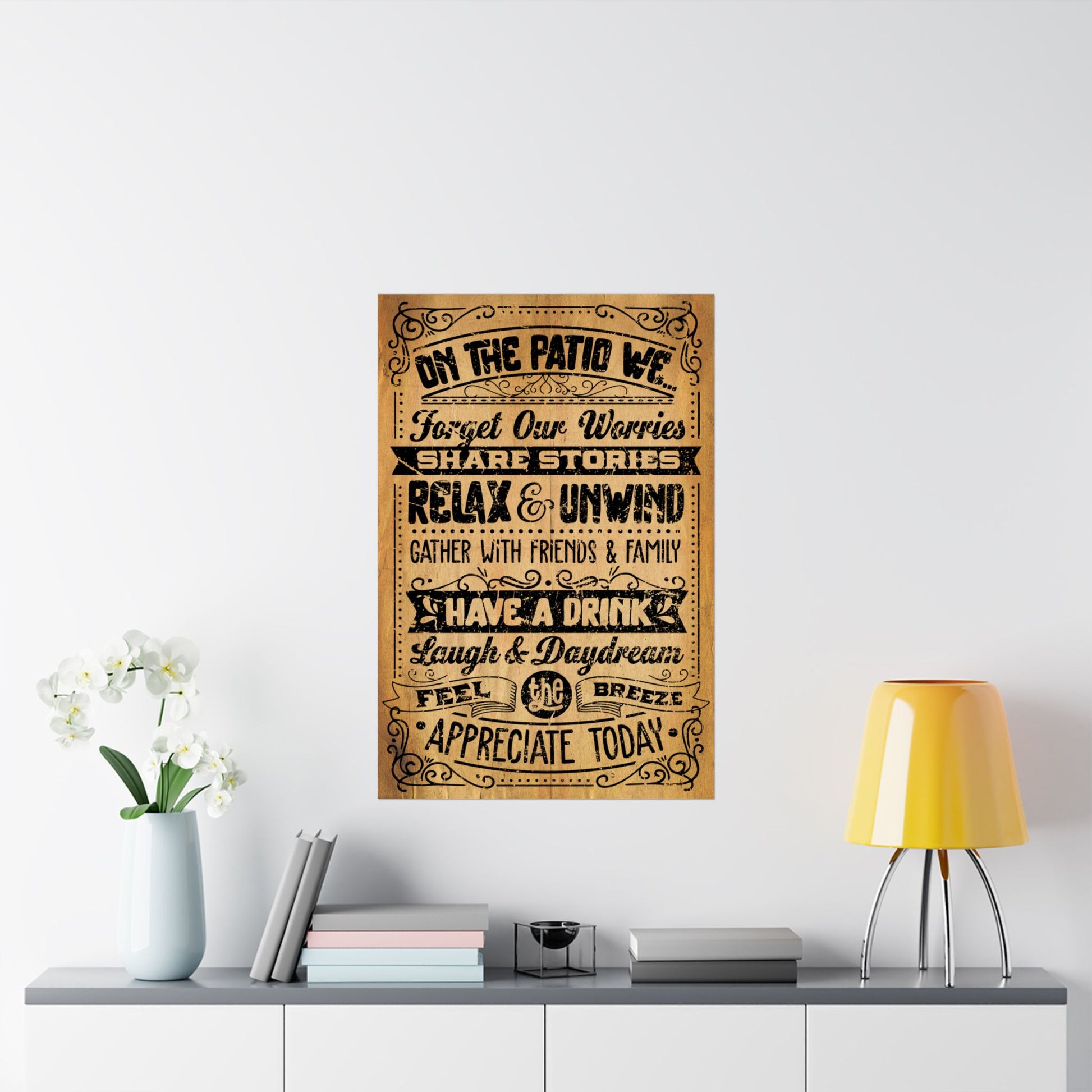 Decorative wall poster with text on a white wall above a shelf with books and a lamp.