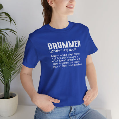 Person wearing a blue t-shirt with a definition of 'drummer' text, standing indoors with a plant in the background.