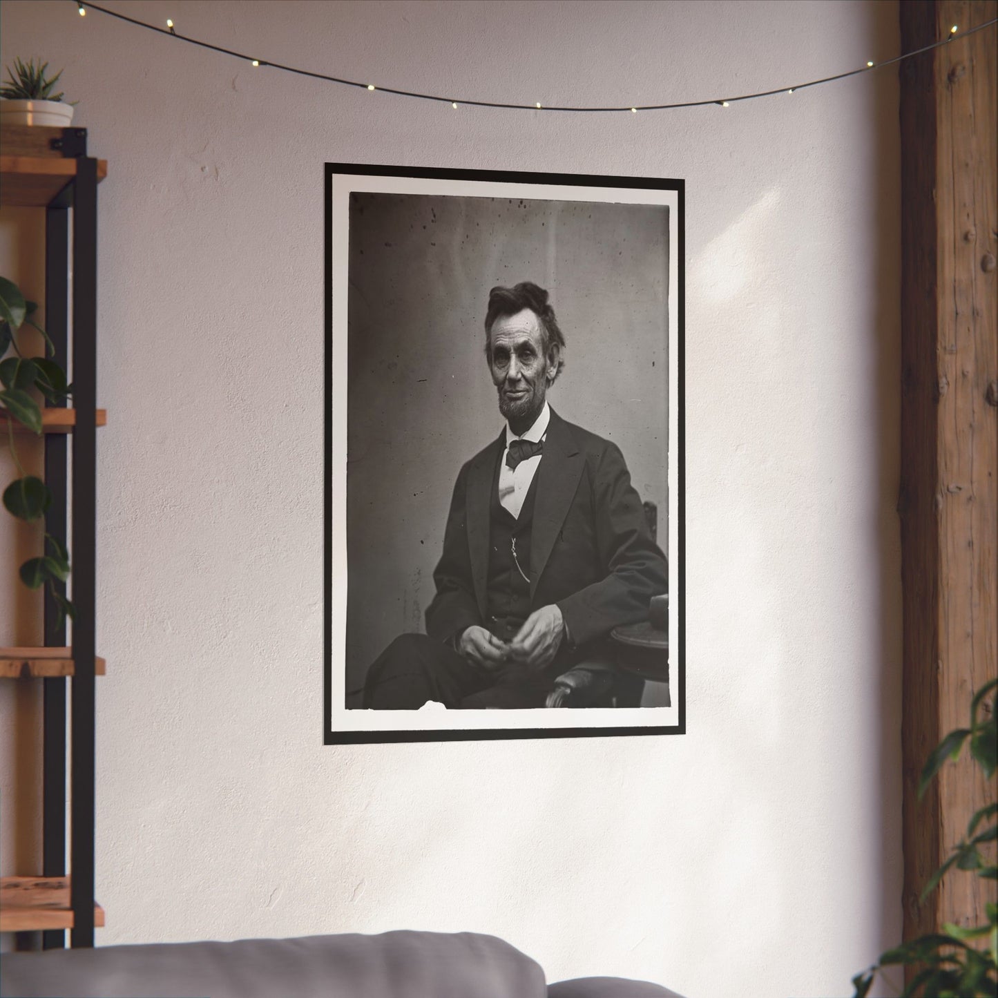Framed portrait of a historical figure on a wall in a room with string lights and a plant.