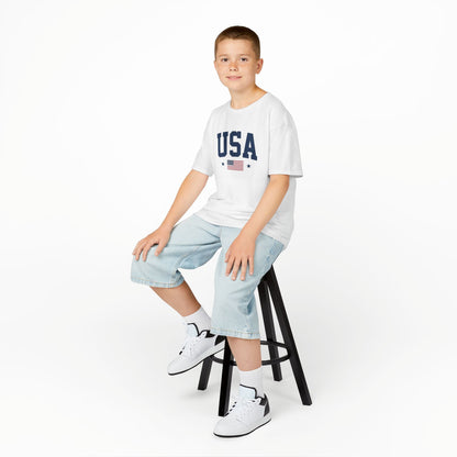 Young person sitting on a stool wearing a white t-shirt with text and graphics, light blue jeans, and white sneakers.