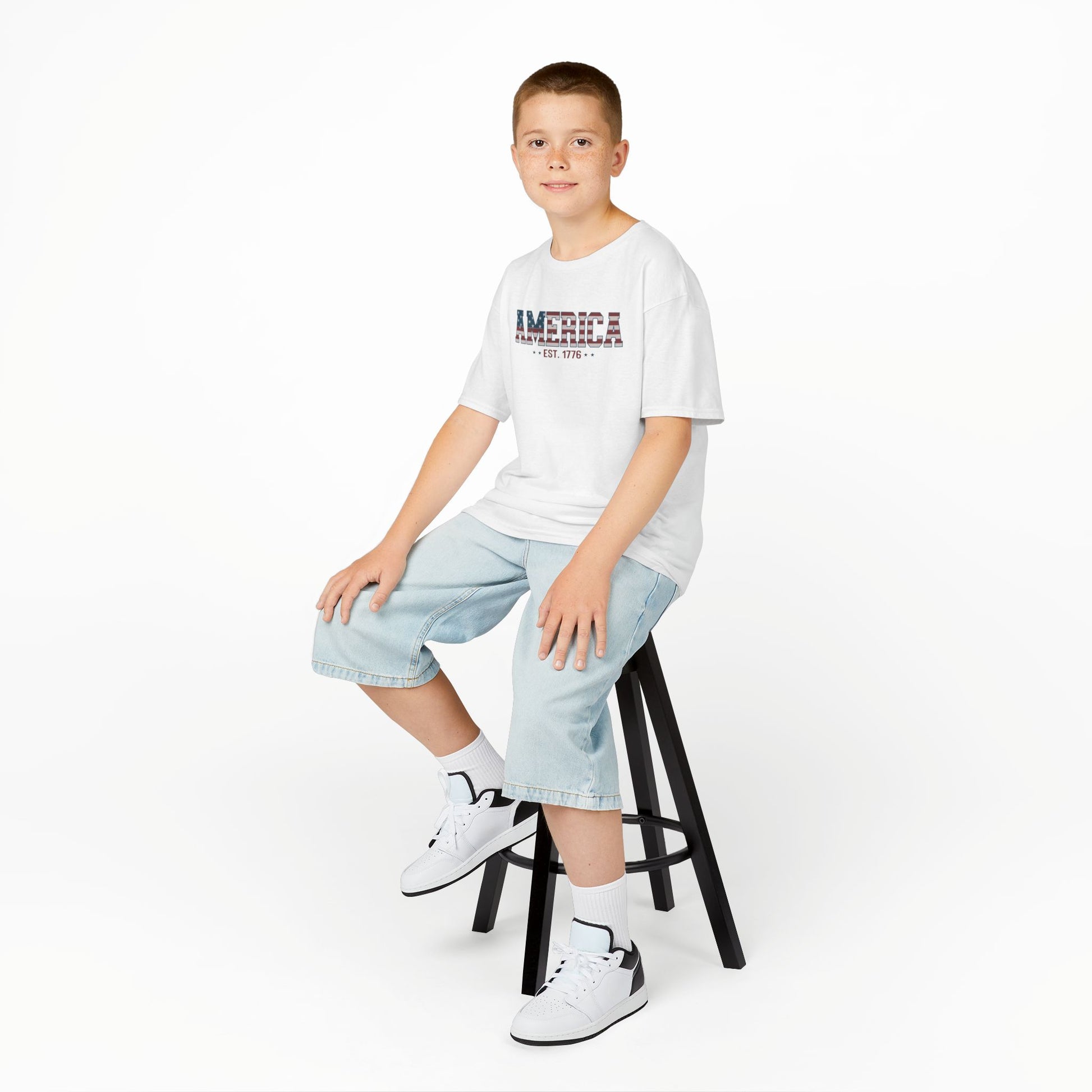 Young person sitting on a stool wearing a white t-shirt and light blue jeans against a white background