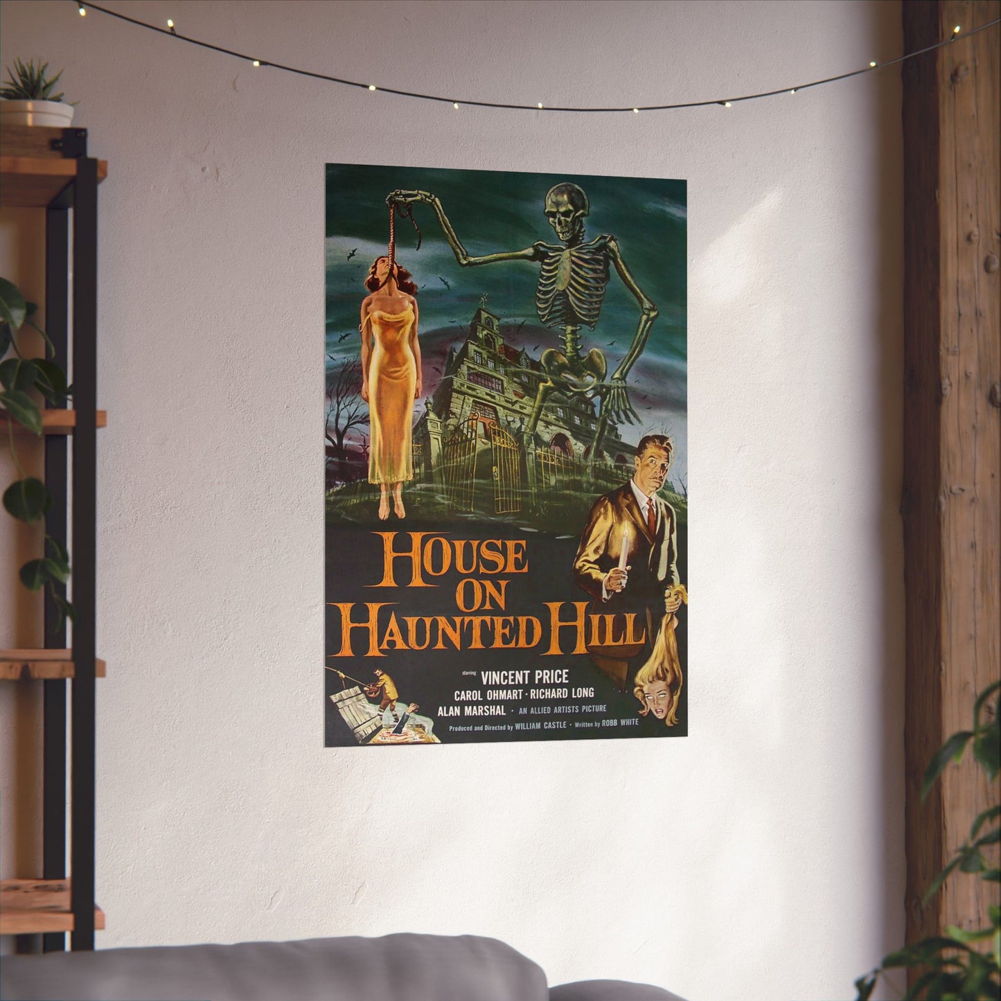 Movie poster for 'House on Haunted Hill' hanging on a wall in a room with a couch and string lights.