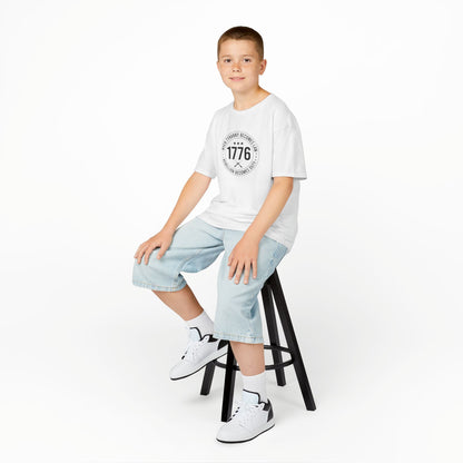 Young person sitting on a stool wearing a white t-shirt and light blue jeans against a white background