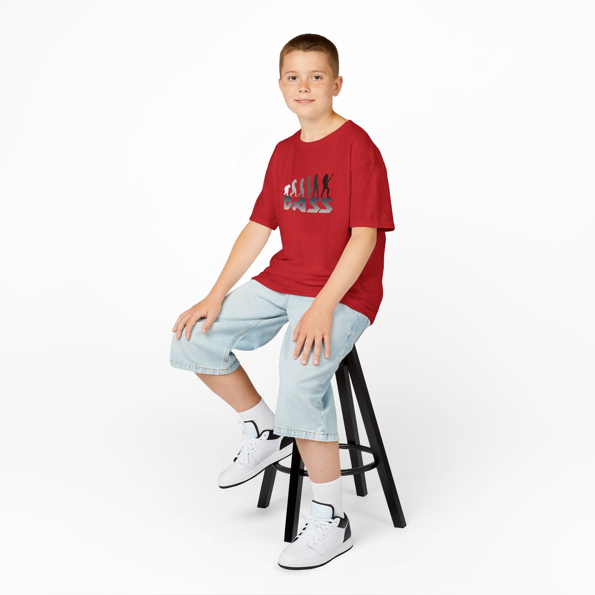 Child wearing a red t-shirt sitting on a stool against a white background