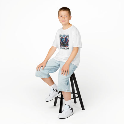 Young person sitting on a stool wearing a white t-shirt with a graphic design, light blue jeans, and white sneakers.