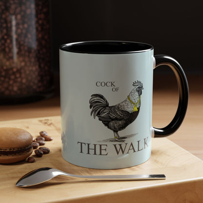 Mug with rooster design and text 'Cock of the Walk' on a wooden surface with coffee beans and a spoon.