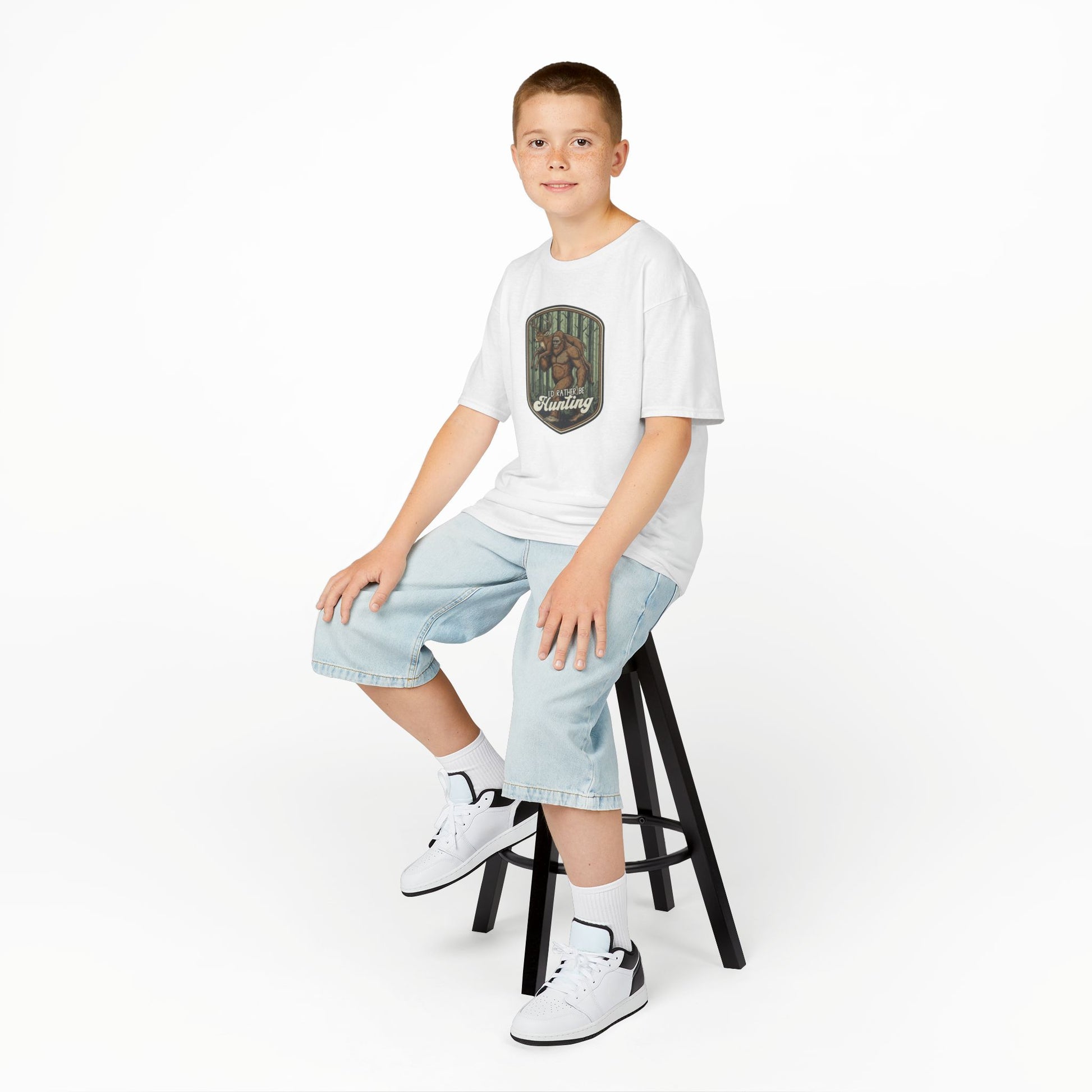 Young boy sitting on a stool wearing a white t-shirt with a graphic design and light blue jeans.
