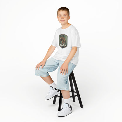 Young boy sitting on a stool wearing a white t-shirt with a graphic design and light blue jeans.