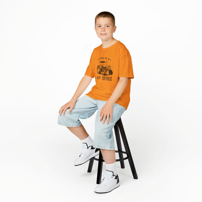 Child sitting on a stool wearing an orange t-shirt with text and graphics, light blue shorts, and white sneakers.
