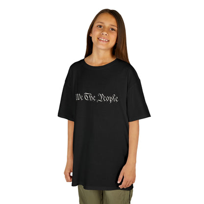 Young girl wearing a black t-shirt with 'We The People' printed on it against a white background
