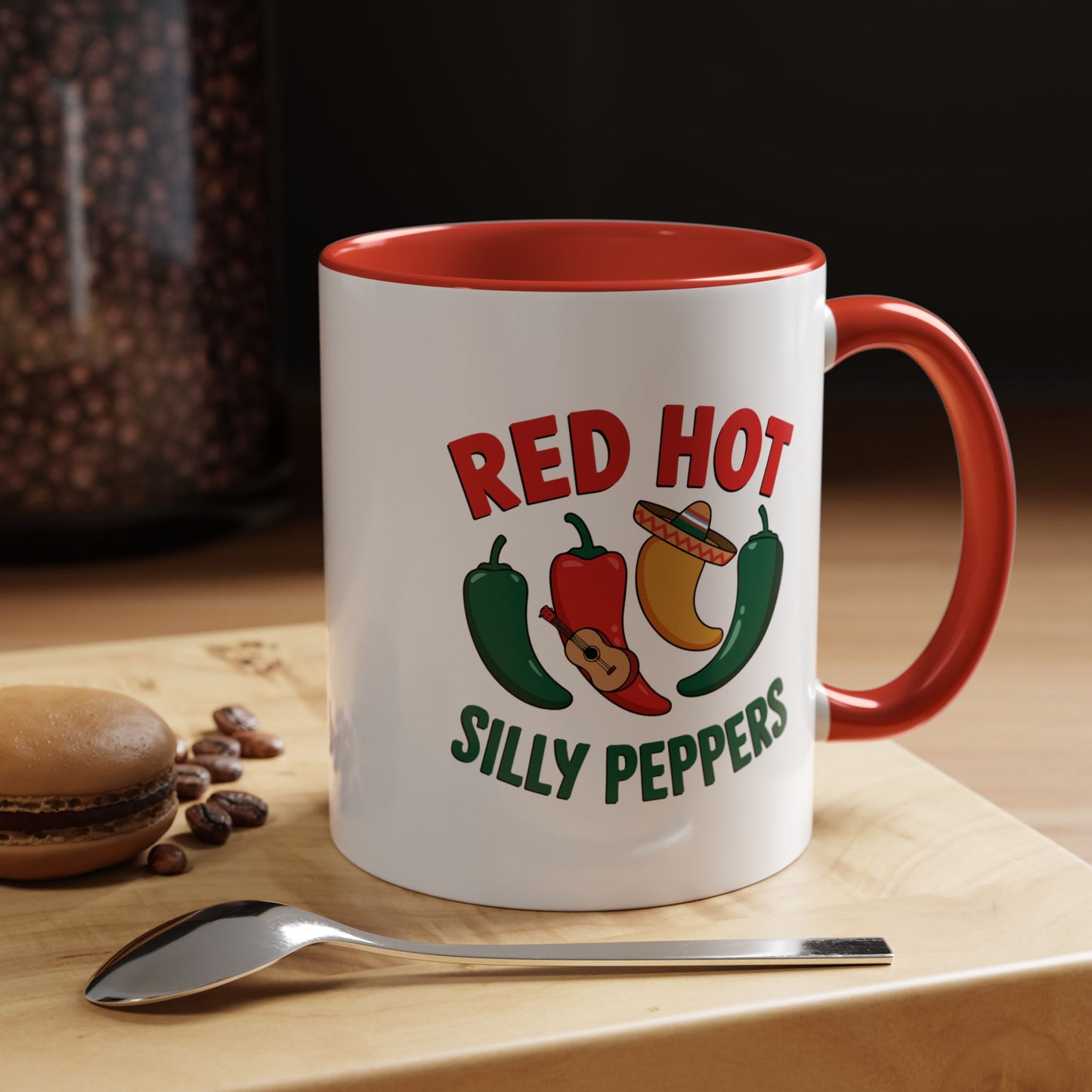White mug with red interior and handle, featuring 'Red Hot Silly Peppers' design, on a wooden surface with coffee beans and a spoon.