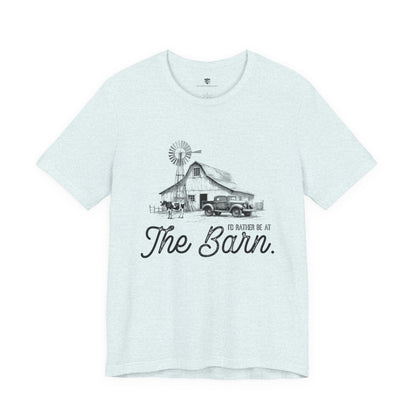 Light blue t-shirt with a graphic of a barn and truck, and text 'I'd rather be at The Barn', on a white background.