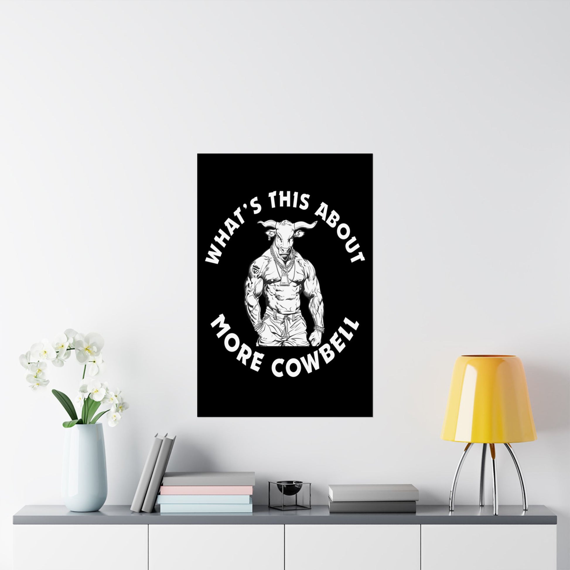 Poster with a graphic of a muscular bull and text 'What's this about more cowbell' on a white wall above a shelf.